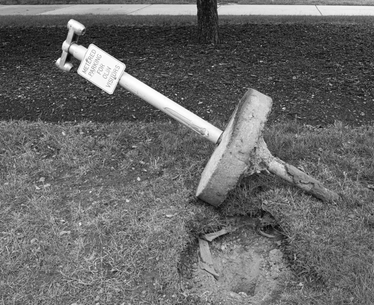 A parking meter torn out of the ground, laying on its side.
