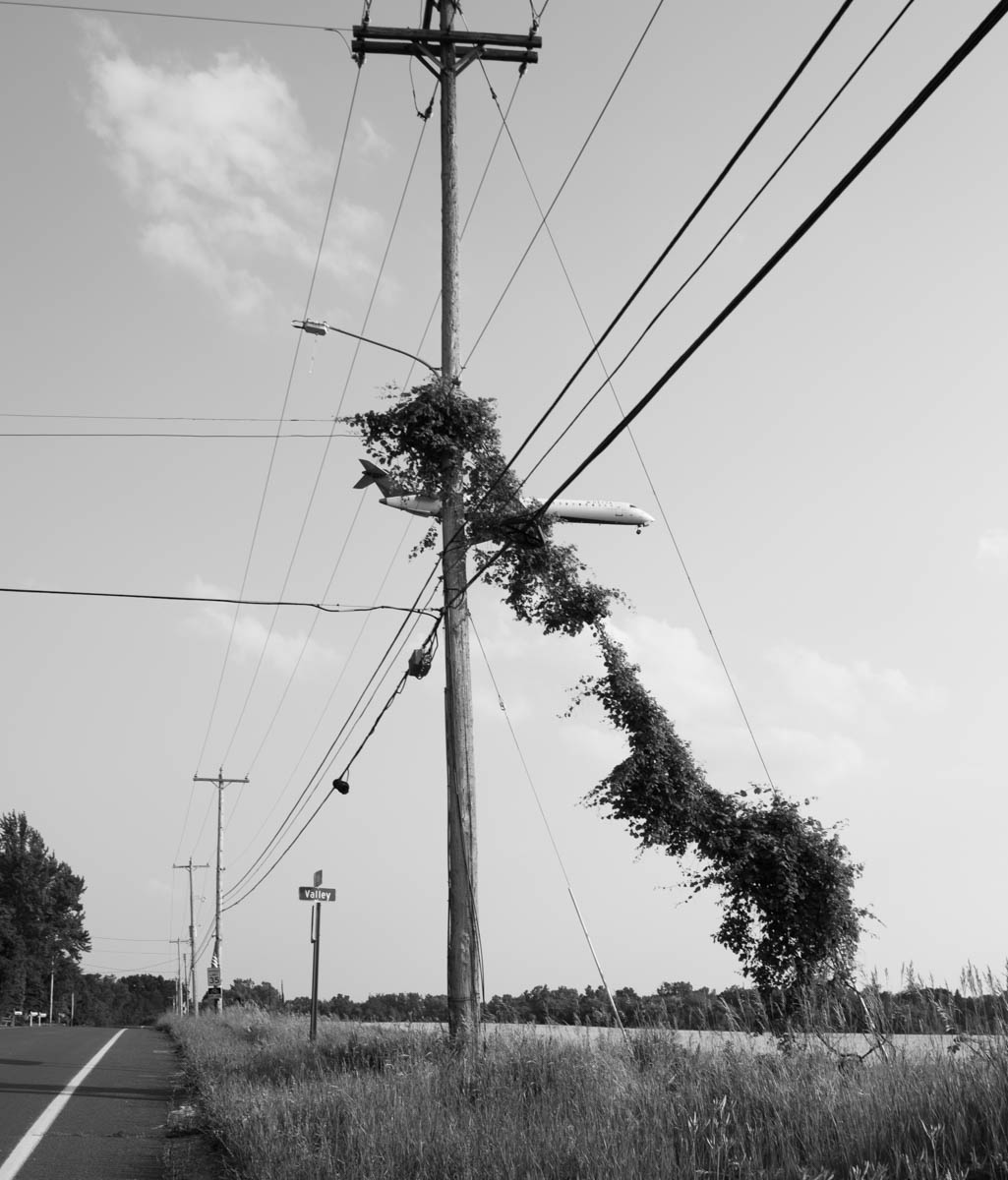 Airplane flying behind wires and pole.